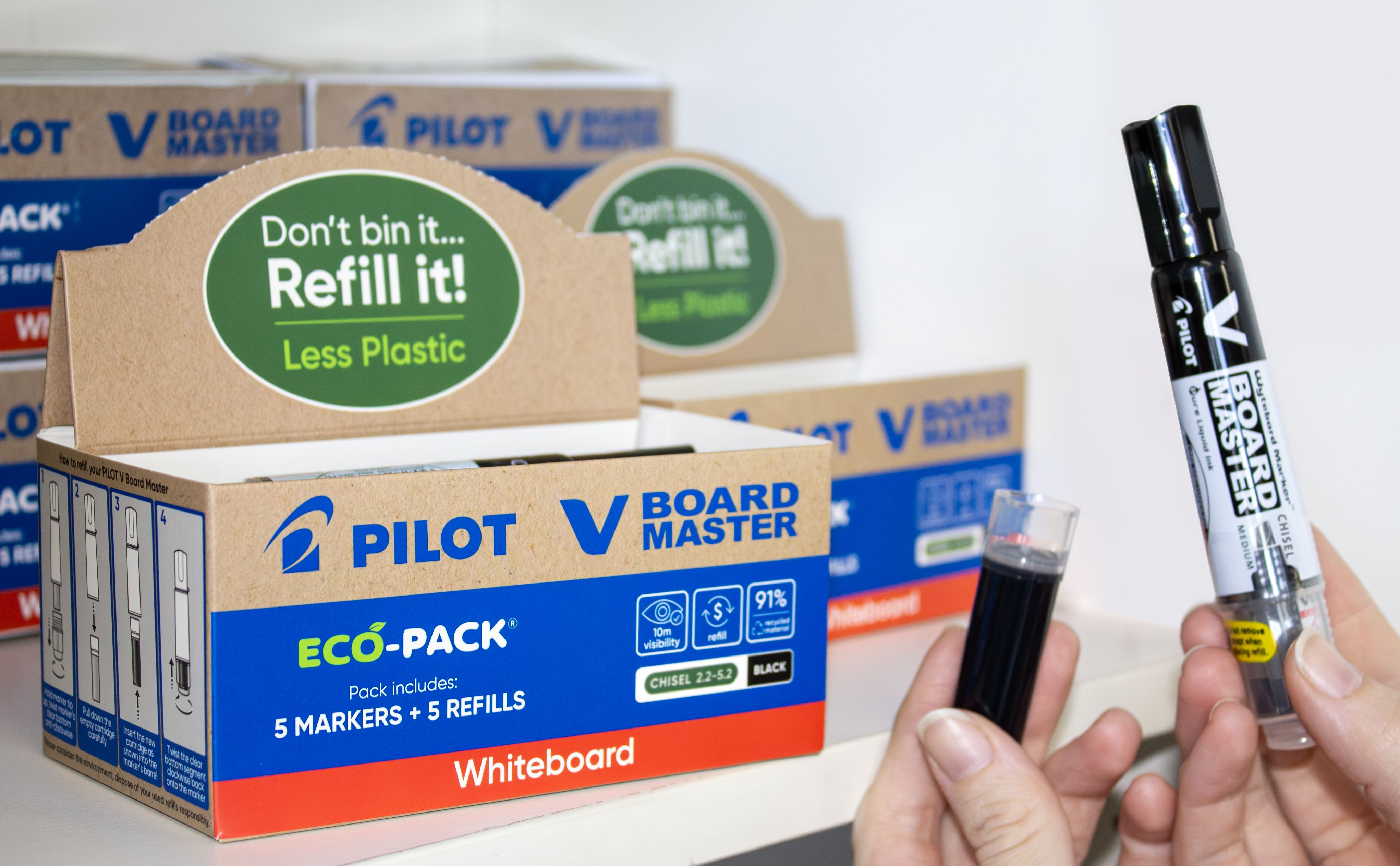 Hand holding a black PILOT V Board Master marker with eco-pack boxes of PILOT V Board also visible