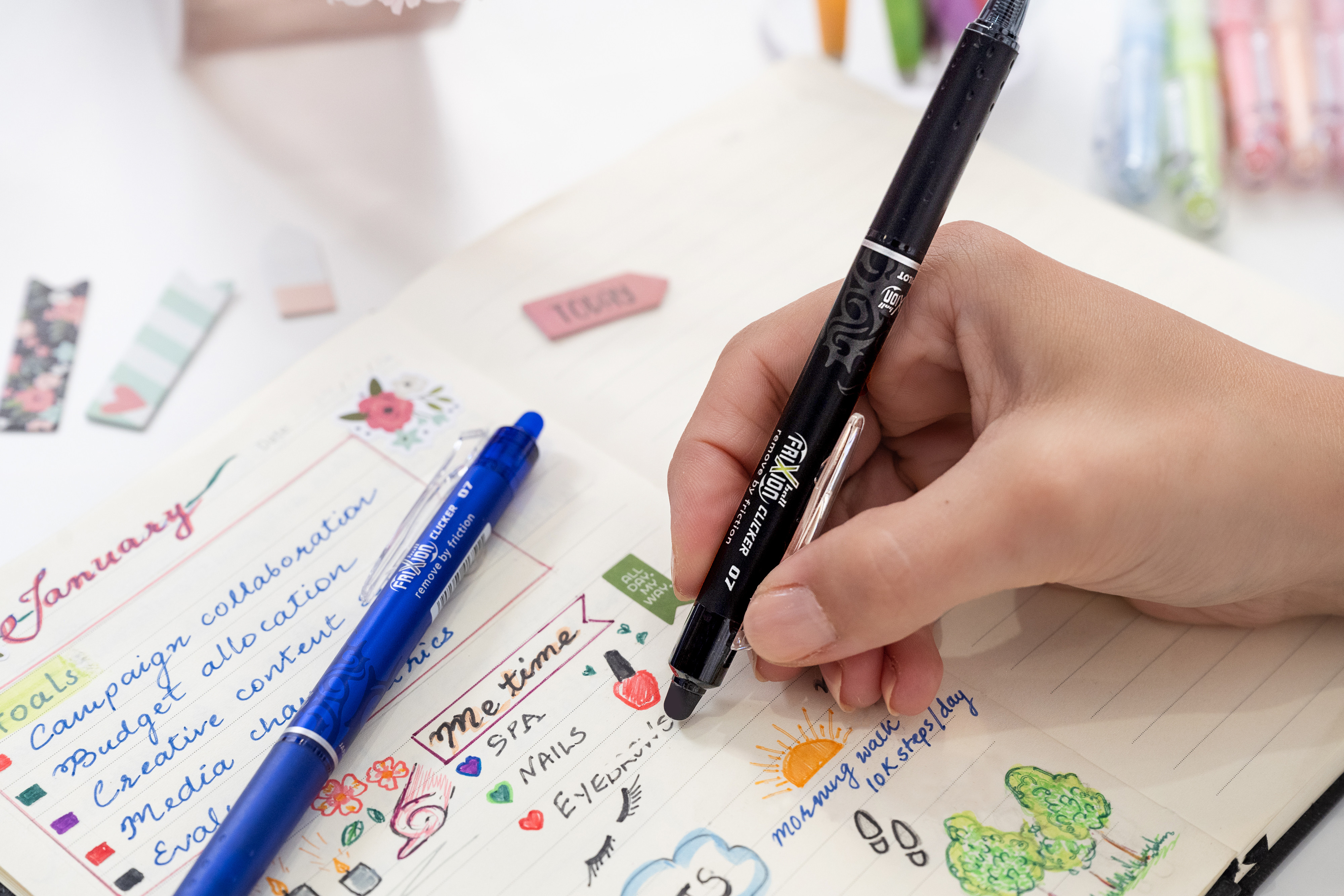 Using a black PILOT FriXion Erasable Clicker pen to decorate a colourful bullet journal layout with drawings, text, and planning notes