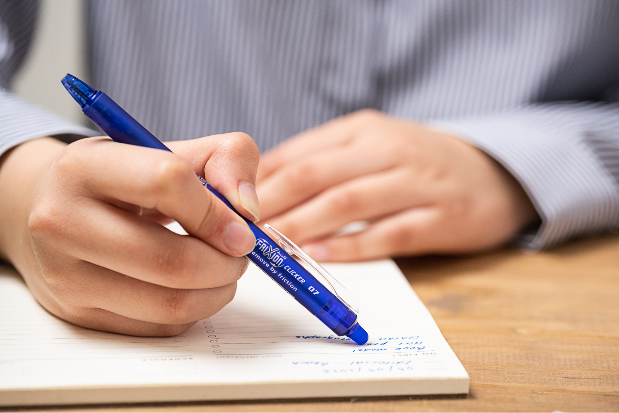 Close-up of a hand writing in a lined notebook with a blue Pilot FriXion pen&mdash;one of the best pens for writing