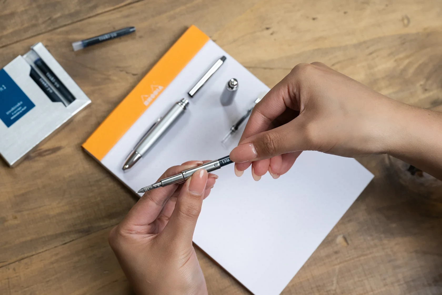 A PILOT Capless Silver Accent Fountain pen being refilled with an iroshizuku Ink Cartridge in shade tsuki-yo.