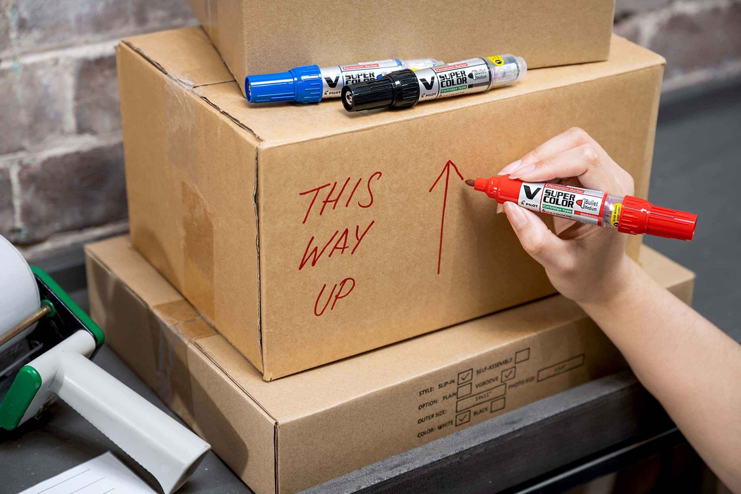 V Super Color Permanent Marker in red writing &ldquo;This Way Up&rdquo; on a cardboard box. 