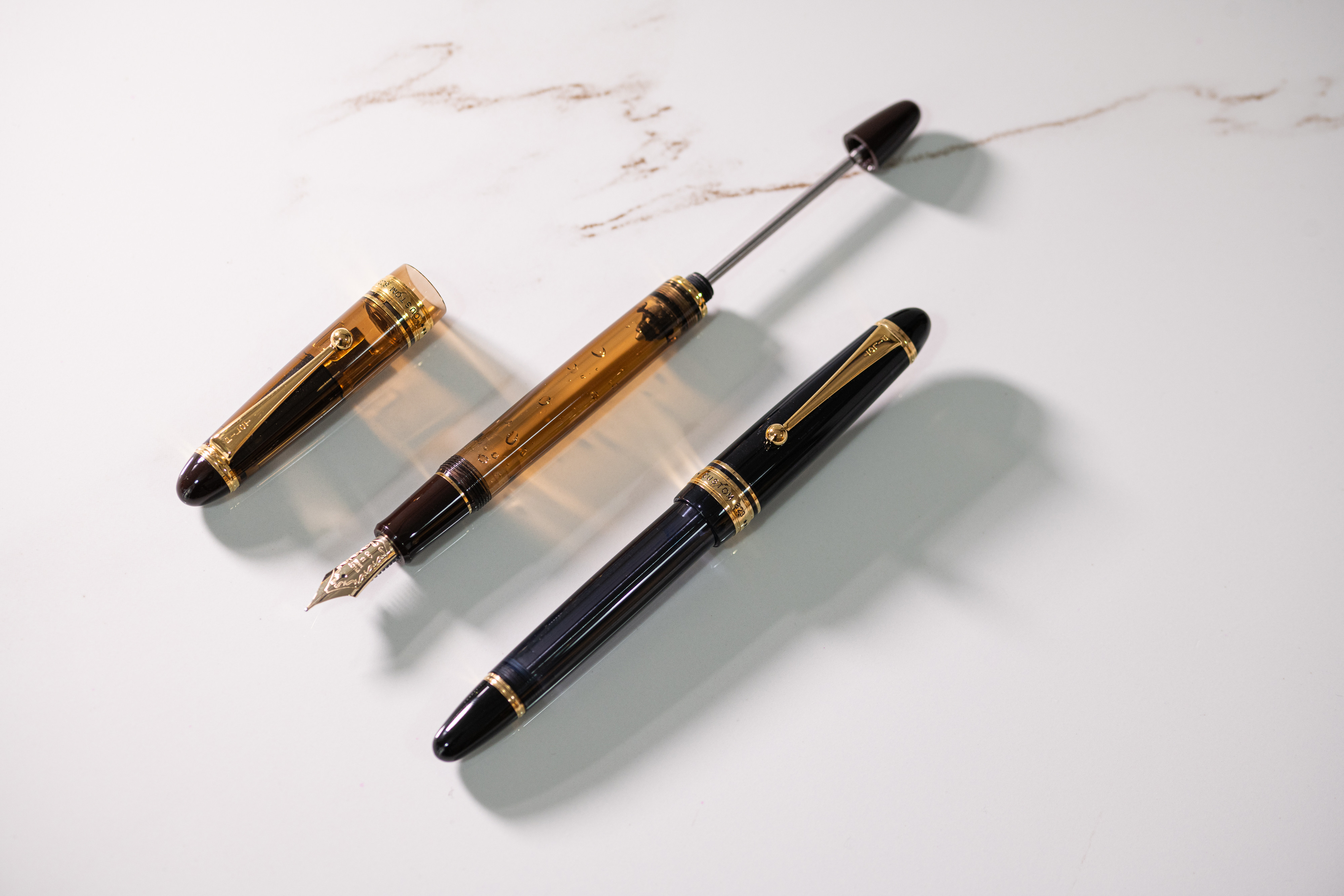 Two CUSTOM 823 vacuum filler fountain pens showing an empty pen barrel before refilling with ink and screwing down the piston