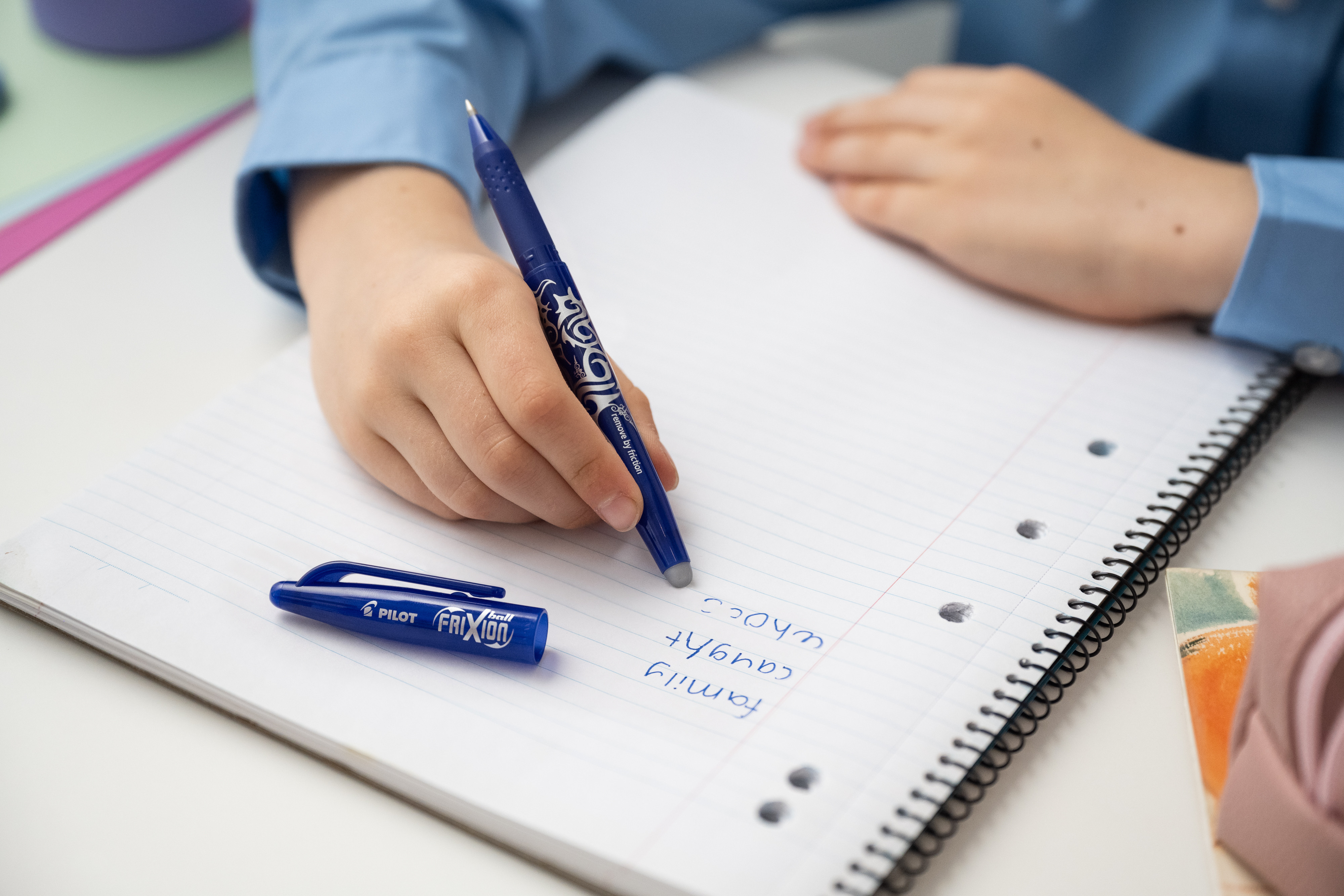 A young person using a blue erasable FriXion pen to ersable a mistake on their school book