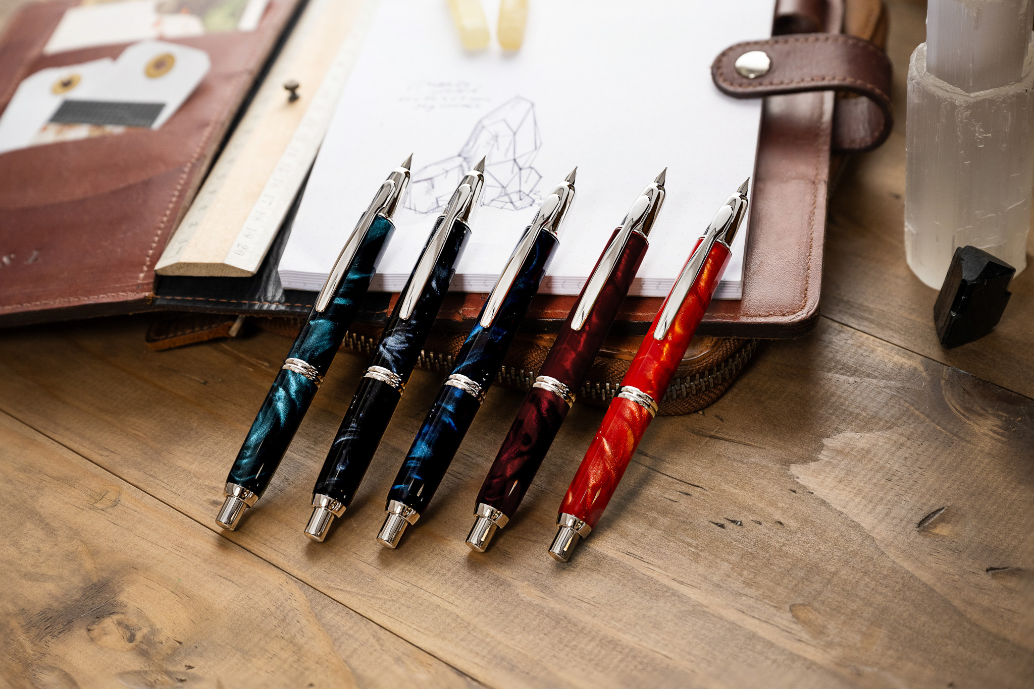 Pilot Capless SE fountain pens in marbled finishes displayed on a wooden desk with an open leather journal