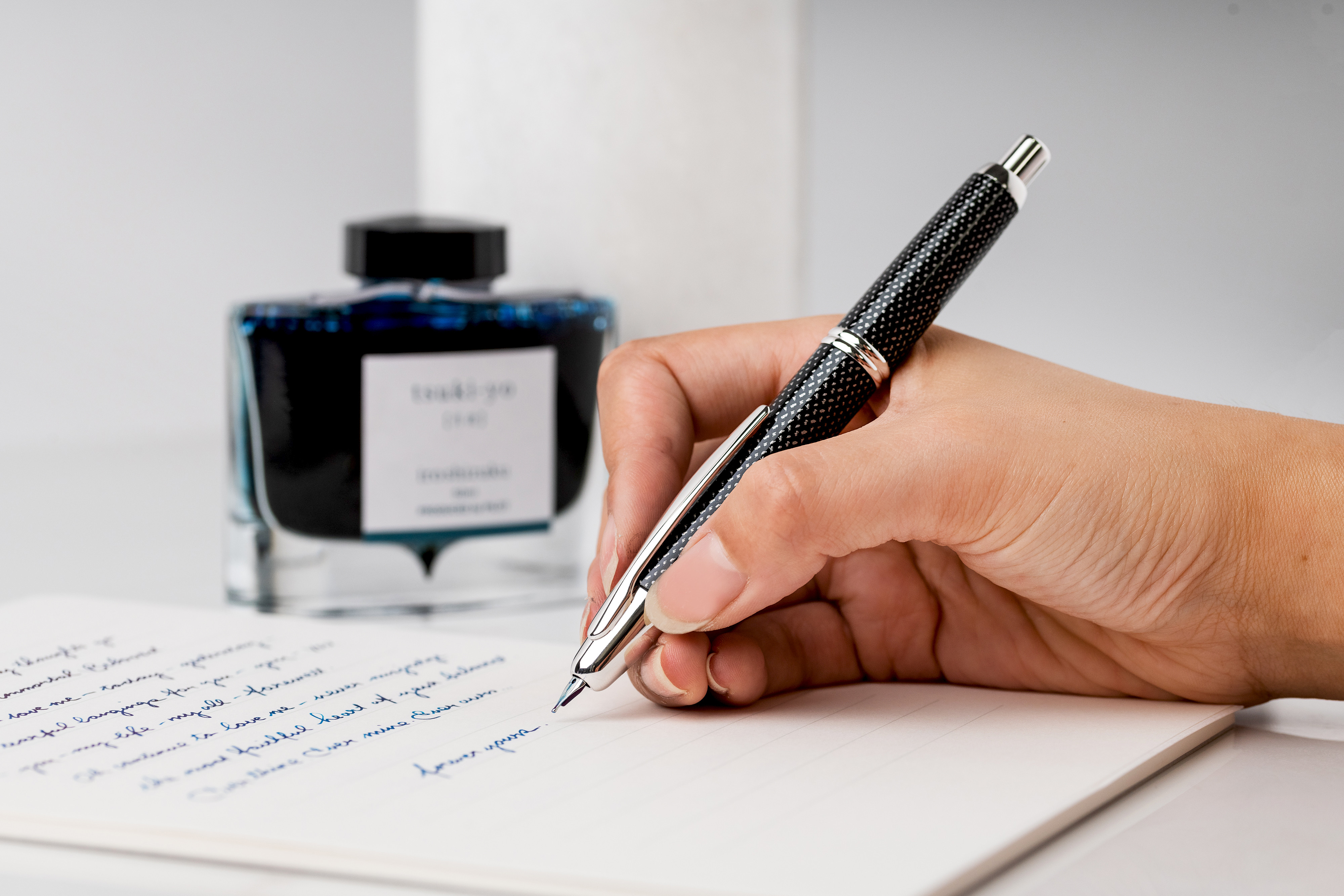 Pilot Capless fountain pen writing in a notebook with Iroshizuku tsuki-yo ink bottle in the background