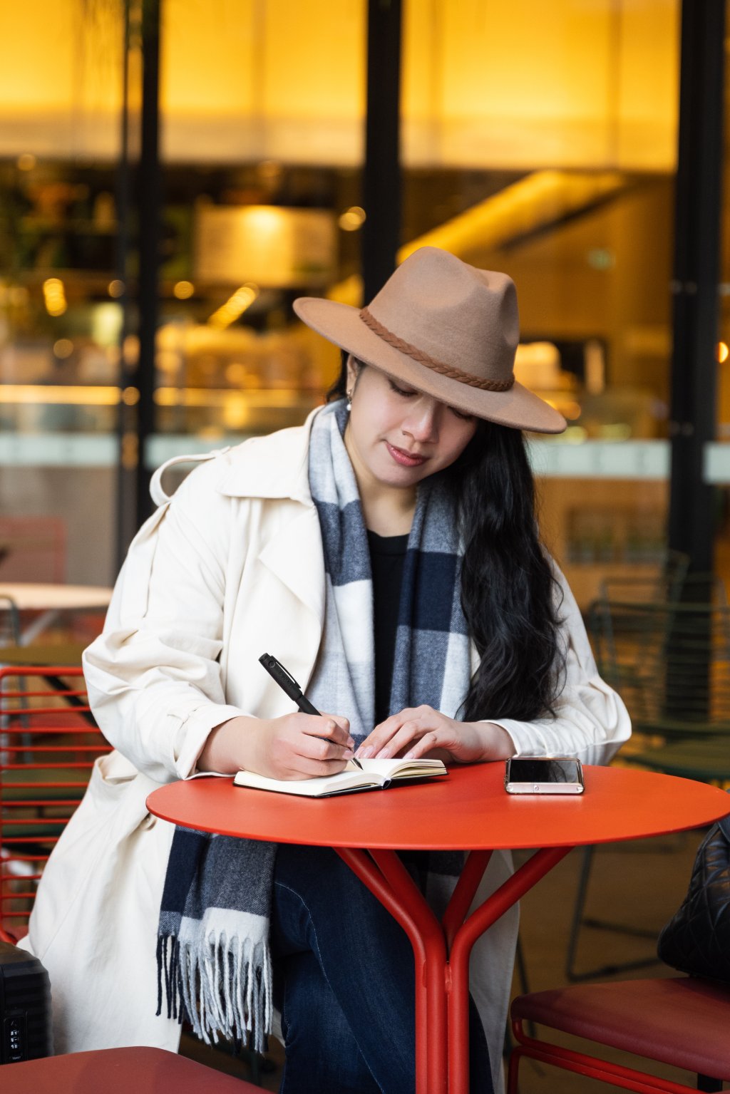 Woman writing with pen and paper at a caf&eacute; table, choosing analogue tools over digital in a modern setting.