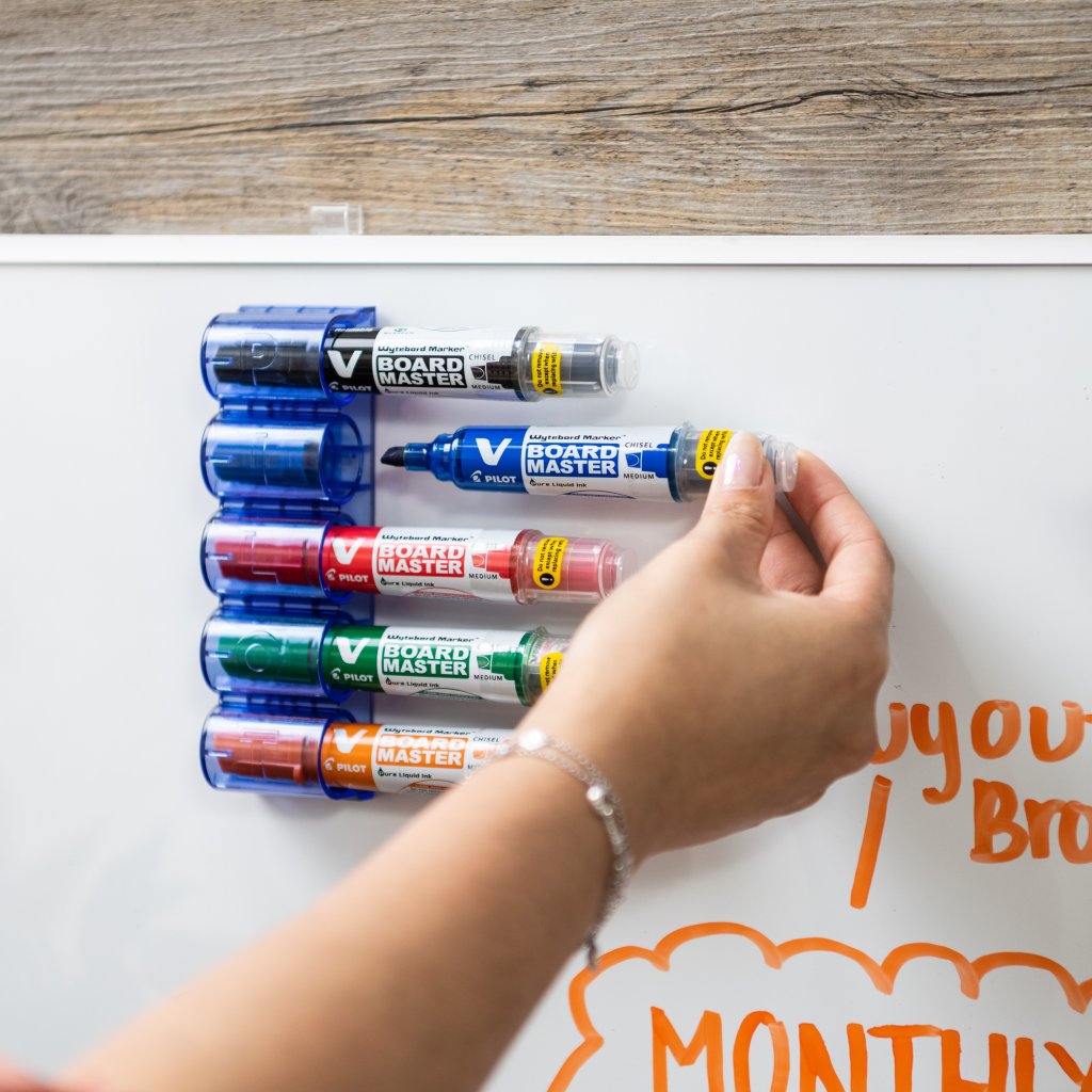 set of 5 V Board Master magnetic whiteboard markers attached to whiteboard being selected to used for writing.