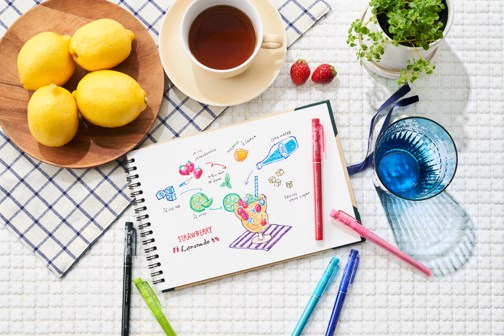 Colourful FriXion pens used to sketch a strawberry lemonade recipe in a notebook, one of the best pens for journaling and note taking.