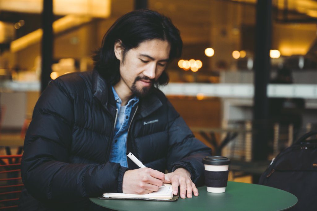 man sitting at a caf&eacute; mindfully writing down yearly goals with his premium fountain pen.