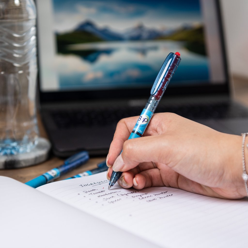 Gel Rollerball Begreen B2P by PILOT Pen writing in a copy book in front of a laptop.